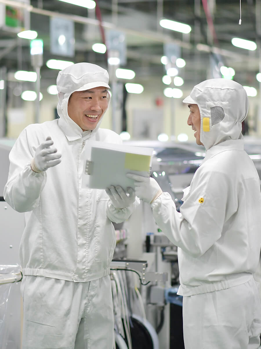 工場で他の人と話す白い防護服を着た人