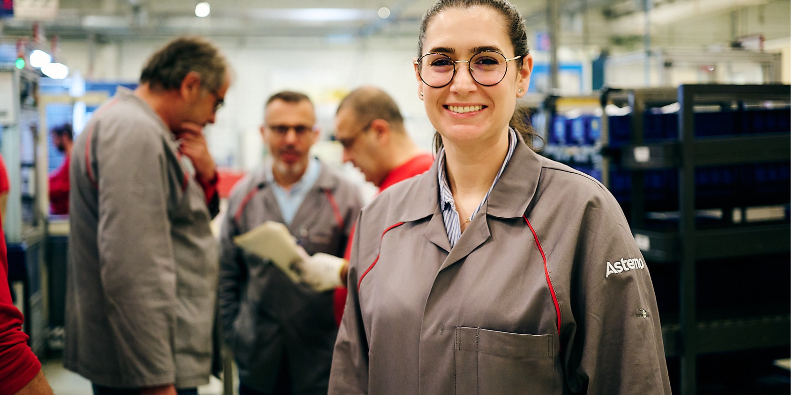 Ein Mitarbeiter steht in einer Produktionsstätte, während Kollegen im Hintergrund arbeiten.