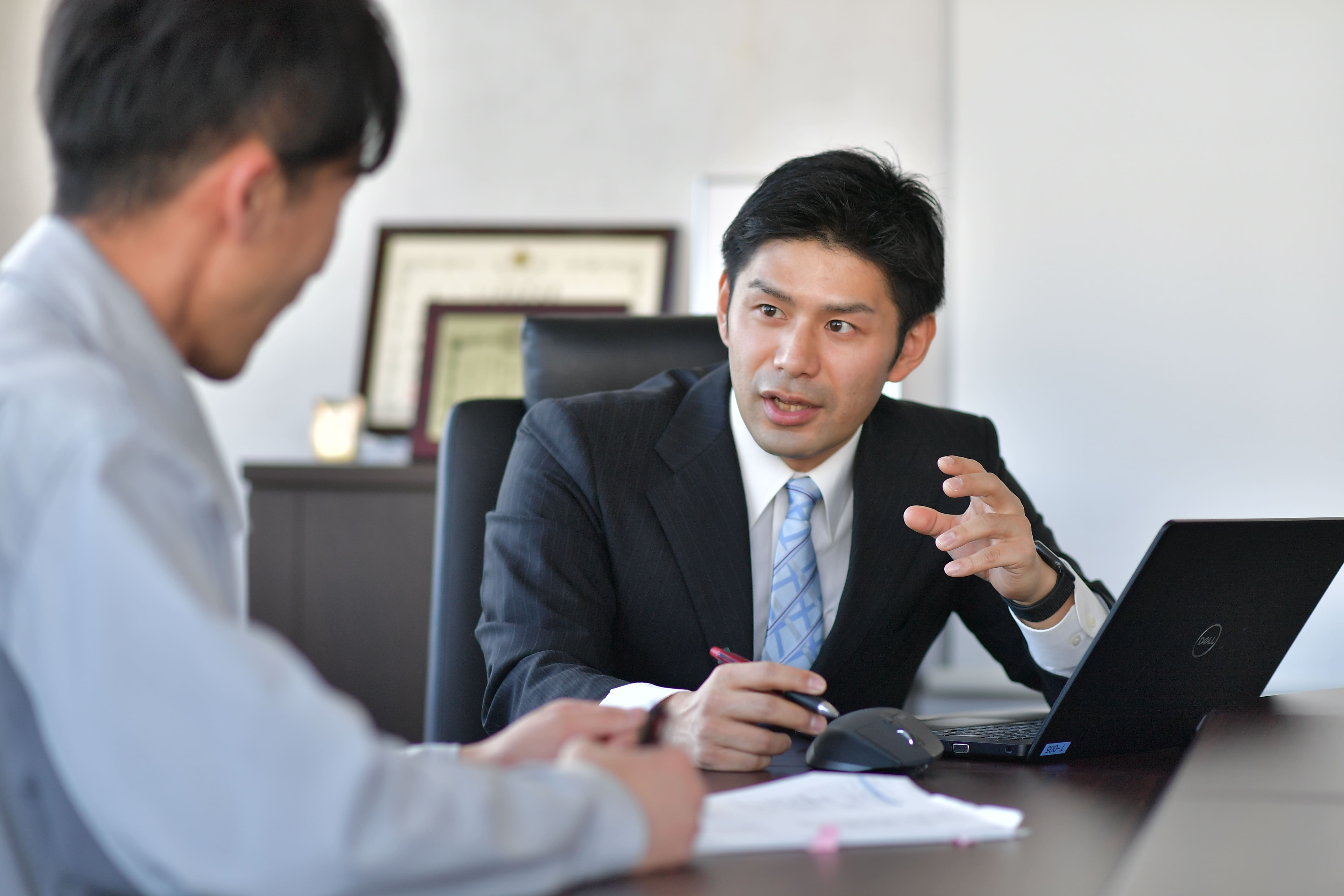 a person in suit sitting at a table with a laptop and a person in a suit