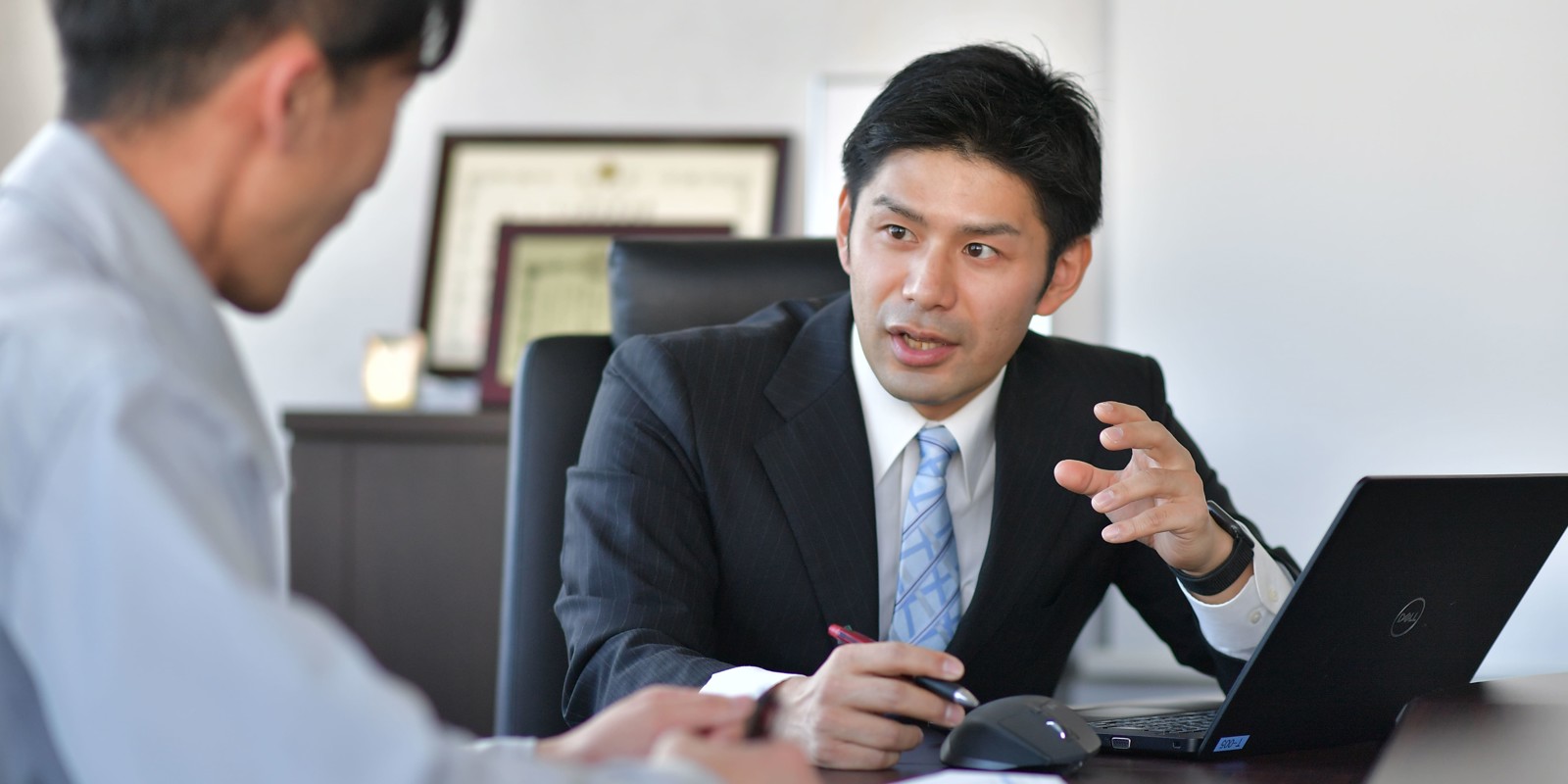 a person in suit sitting at a table with a laptop and a person in a suit