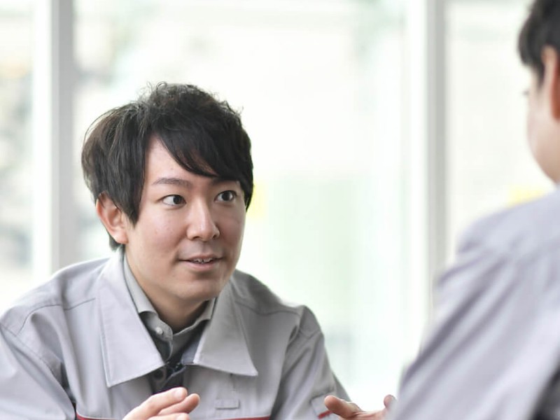 灰色のオーバーオールを着た人が他の人と話している