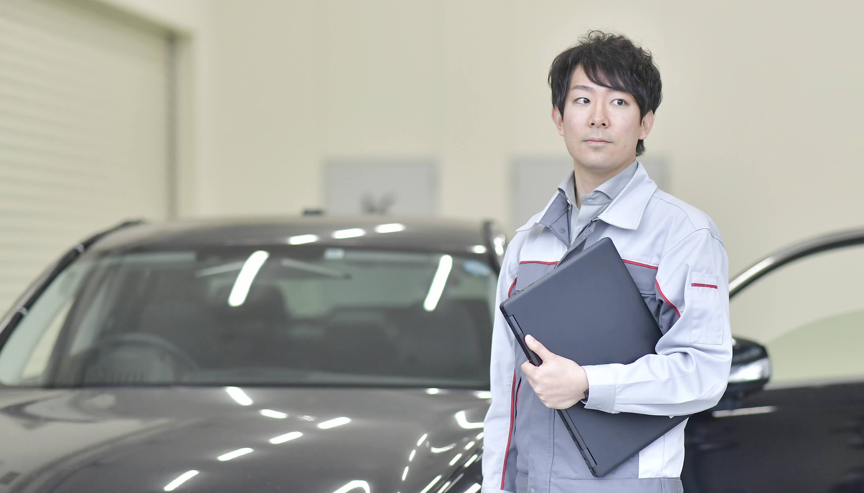 ノートパソコンを持ち、車の前に立っている人