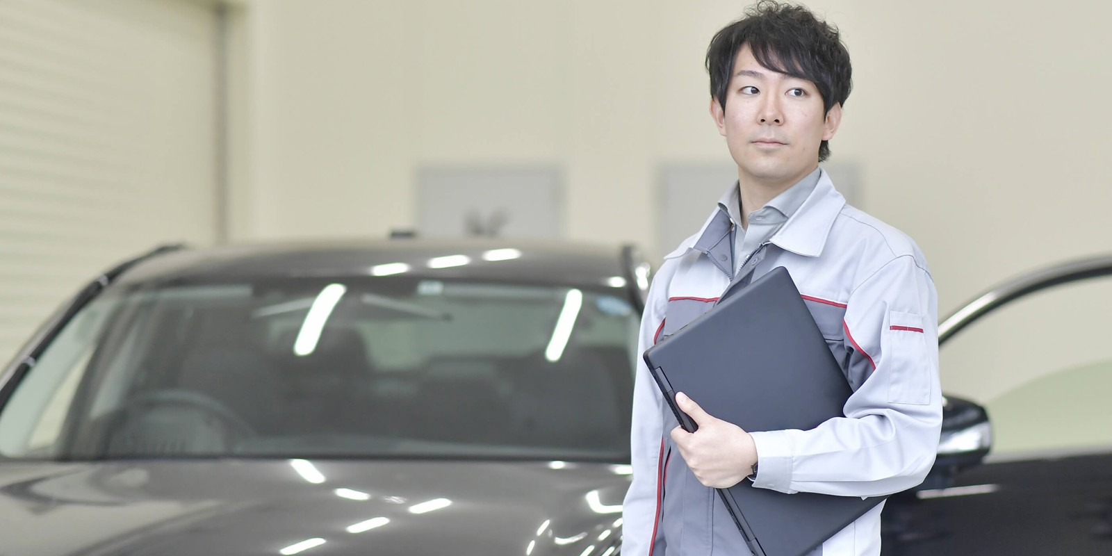 ノートパソコンを持ち、車の前に立っている人